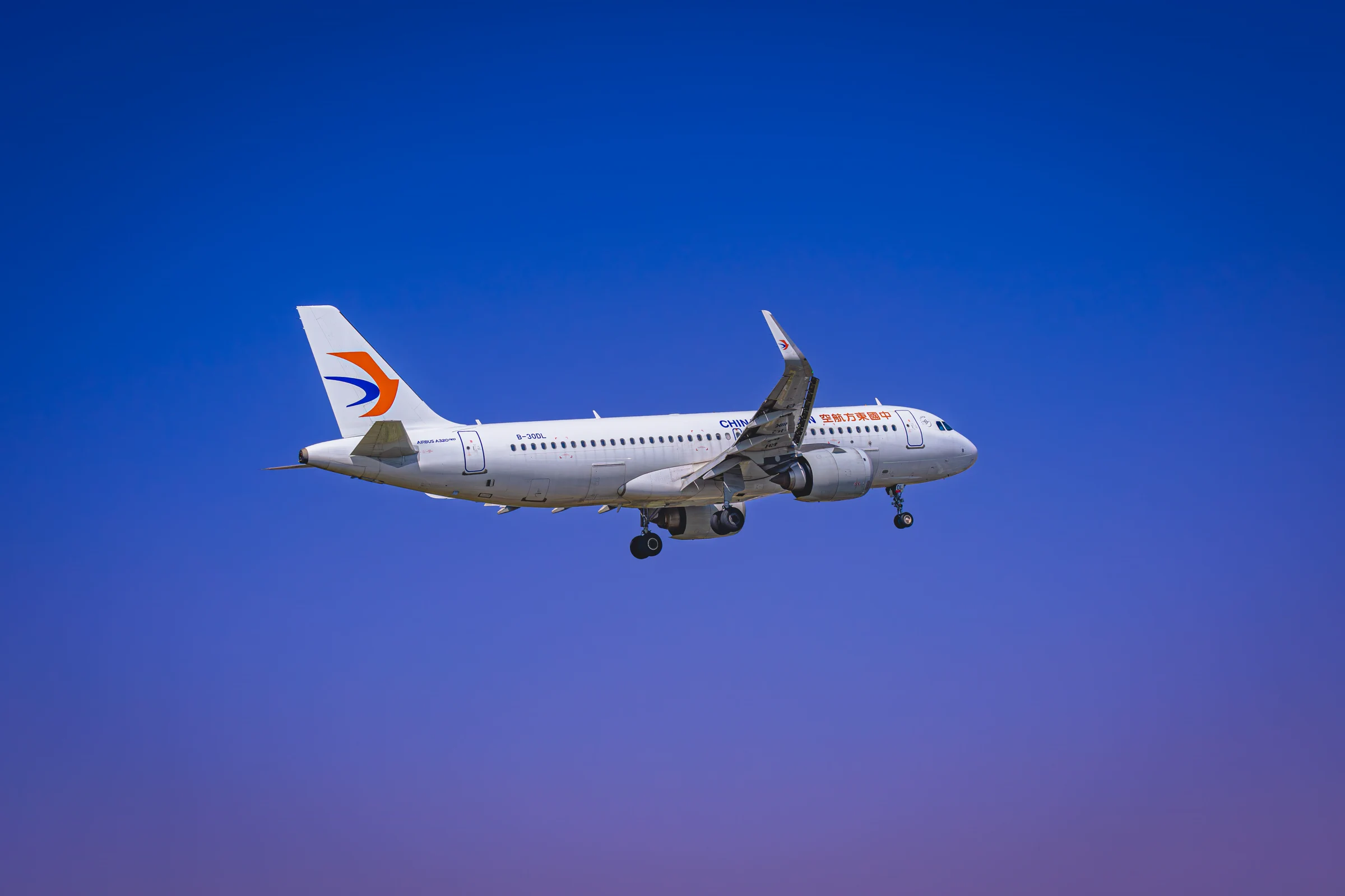 A China Eastern aircraft in flight against a clear blue sky.